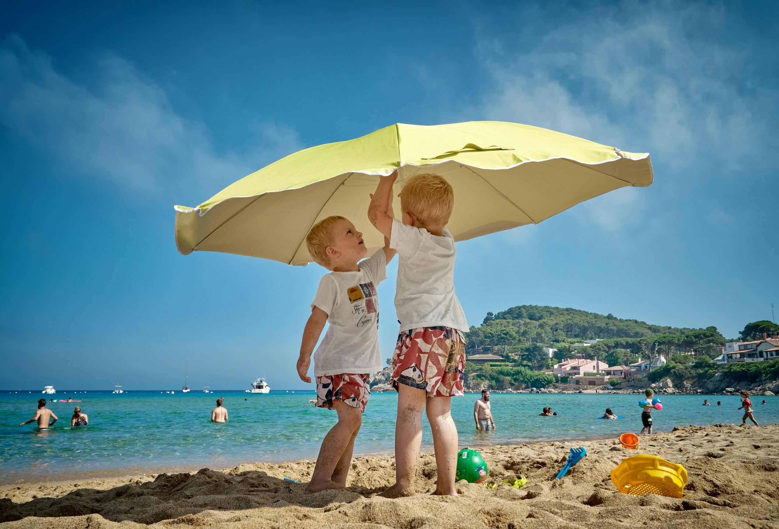 Two boys on the beach putting up an umbrella